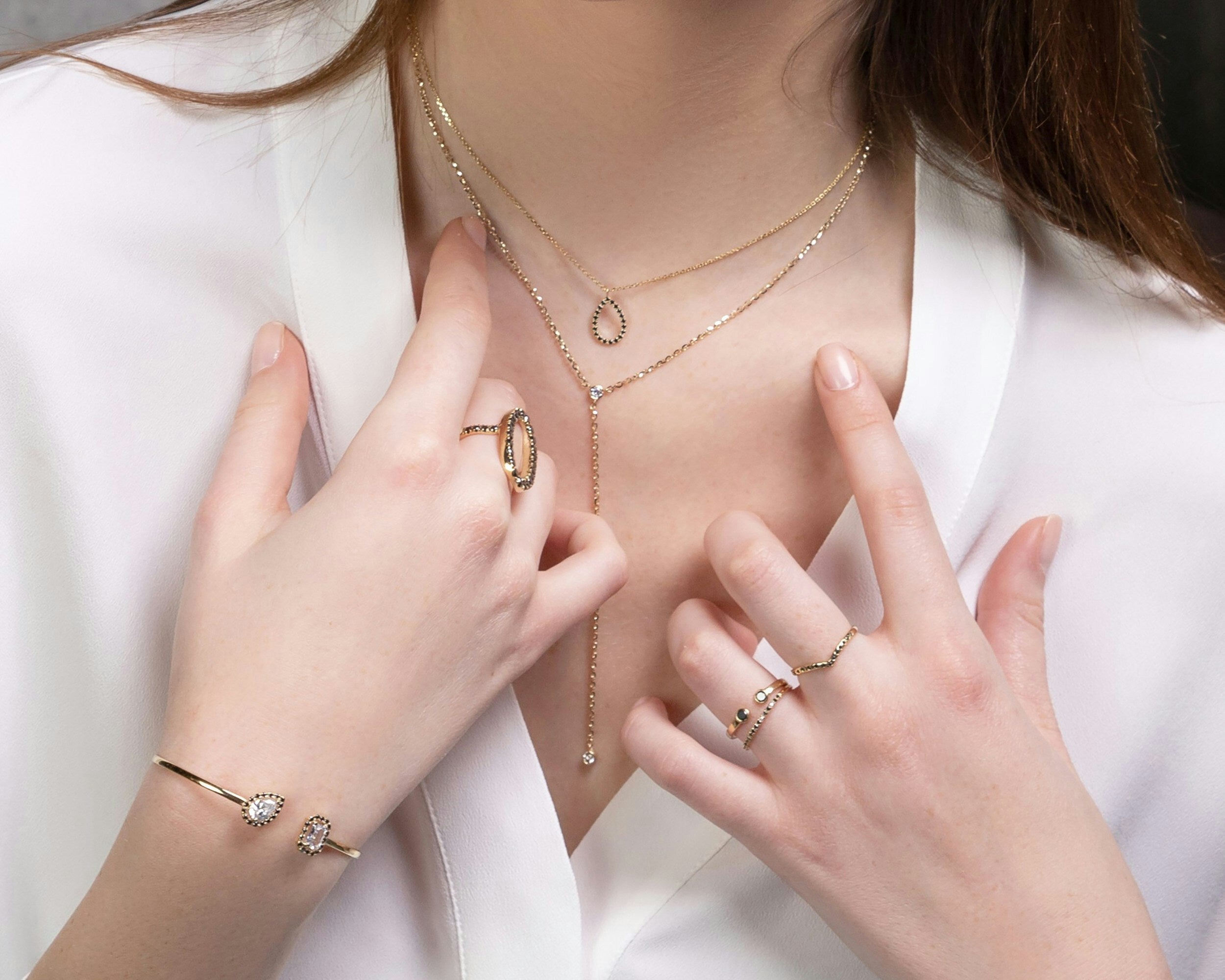 Close-up of a person wearing multiple pieces of gold jewelry including a necklace, rings, and a bracelet.